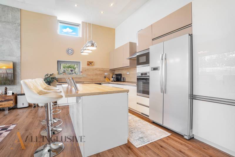 NA PREDAJ NADŠTANDARDNÁ 4-IZB. NOVOSTAVBA, DUN. KLÁTOV - Kuchyňa v rodinnom dome s bielymi skrinkami, barovými stoličkami a vstavanými spotrebičmi.