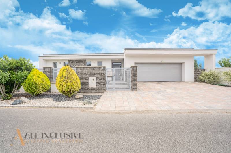 NA PREDAJ NADŠTANDARDNÁ 4-IZB. NOVOSTAVBA, DUN. KLÁTOV - Rodinný dom v Dunajskom Klátove so záhradou a garážou pod modrou oblohou.