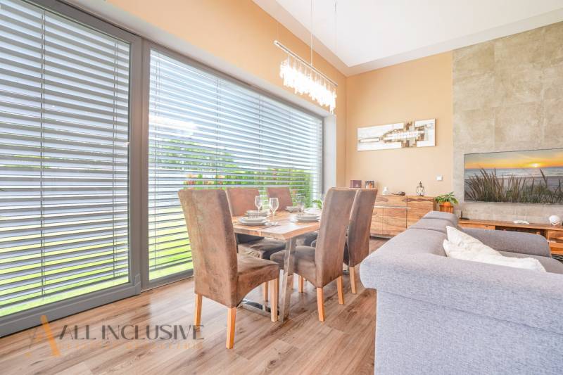 NA PREDAJ NADŠTANDARDNÁ 4-IZB. NOVOSTAVBA, DUN. KLÁTOV - Jedálenský kút v rodinnom dome s dreveným stolom, kreslami a zatemneným oknom.