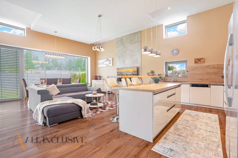 NA PREDAJ NADŠTANDARDNÁ 4-IZB. NOVOSTAVBA, DUN. KLÁTOV - Obývačka v rodinnom dome s kuchyňou, sivou sedačkou a jedálenským stolom.