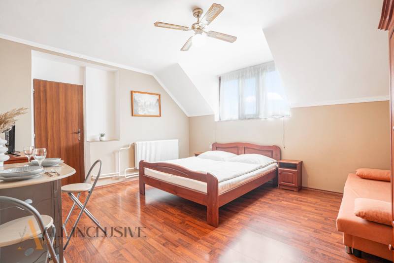 NA PREDAJ PENZIÓN VO VEĽKOM MEDERI – SUNGARDEN - Spálňa v hoteloch a penziónoch s drevenou posteľou, bielym obliečkami a stolom s riadom.