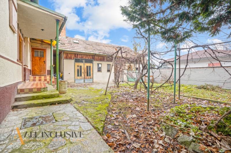 REZERVOVANÉ 4-IZBOVÝ RODINNÝ DOM, TOPOĽNÍKY - Dvor rodinného domu v Topoľníkoch, zelená plocha s opadaným lístím, drevený prístrešok.