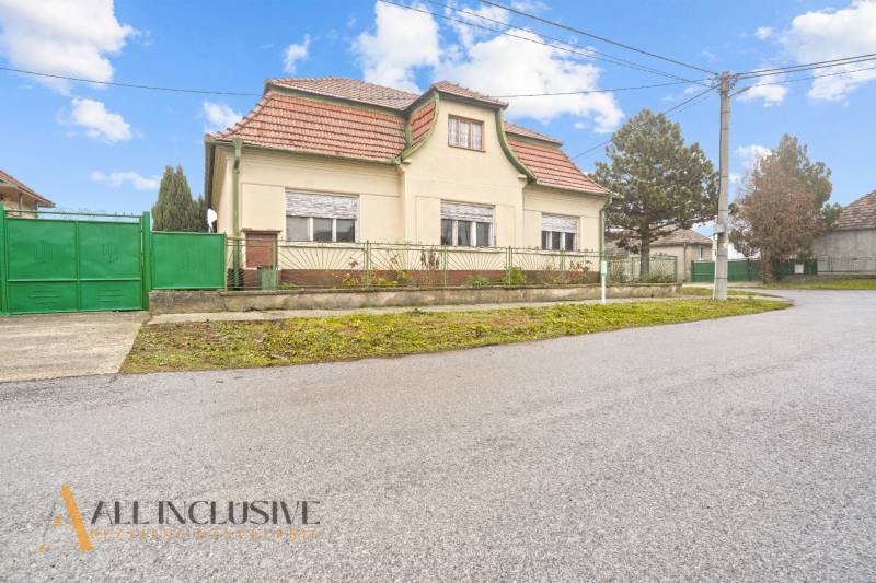 REZERVOVANÉ 4-IZBOVÝ RODINNÝ DOM, TOPOĽNÍKY - Rodinný dom v Topoľníkoch s červenou strechou a zelenou bránou pri ceste.