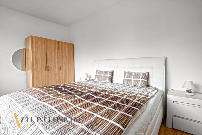 NA PREDAJ APARTMÁNOVÝ DOM VO VEĽKOM MEDERI - Svetlá spálňa s dvojposteľou, šatníkom, nočným stolíkom a podlahou s dreveným dekorom.