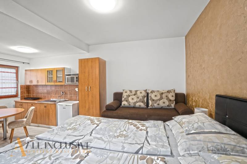 NA PREDAJ APARTMÁNOVÝ DOM VO VEĽKOM MEDERI - Interiér hotelovej izby s kuchynským kútom a podlahou s dreveným dekorom.