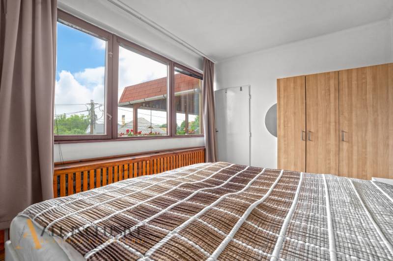 NA PREDAJ APARTMÁNOVÝ DOM VO VEĽKOM MEDERI - Spálňa s veľkým oknom, drevenou skriňou a posteľou v hoteloch a penziónoch.