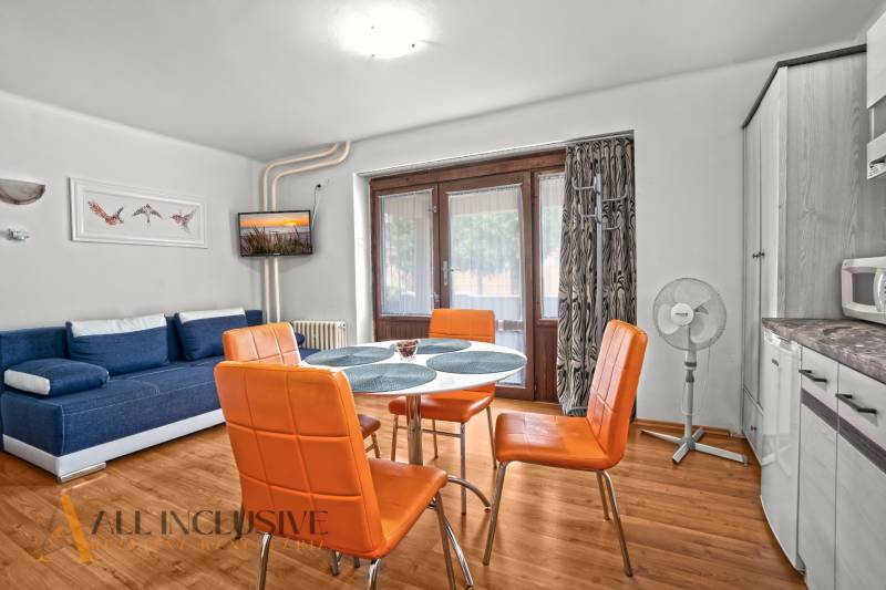 NA PREDAJ APARTMÁNOVÝ DOM VO VEĽKOM MEDERI - Svetlá izba s oranžovými stoličkami, modrým gaučom a podlahou s dreveným dekorom.