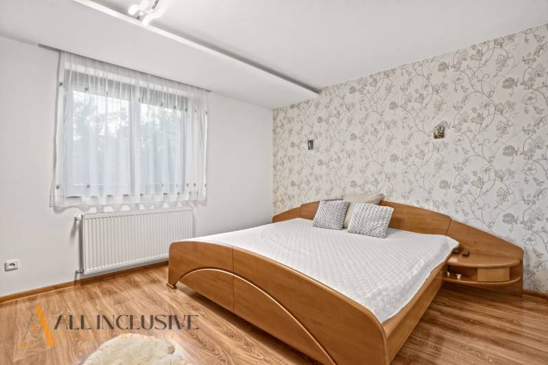 NA PREDAJ 6-IZBOVÝ POSCH. RODINNÝ DOM, HORNÉ SALIBY - Spálňa v rodinnom dome s posteľou a podlahou s dreveným dekorom. Tapeta s kvetinovým vzorom.