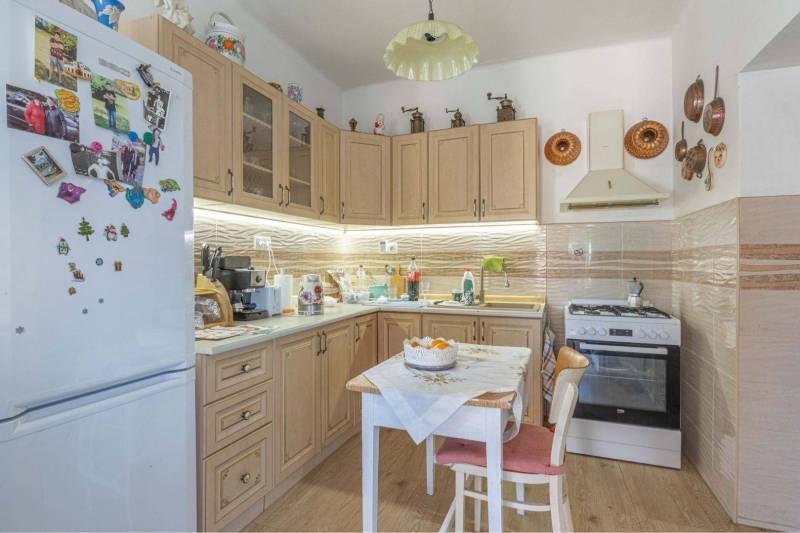 ZĽAVA - 3 IZBOVÝ RODINNÝ DOM, BLÍZKO CENTRA DUN.STREDY - Kuchyňa v rodinnom dome so svetlými skriňami, dekorovaná podlaha a stôl so stoličkami.