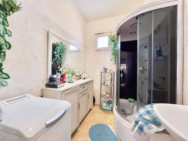 ZĽAVA - 3 IZBOVÝ RODINNÝ DOM, BLÍZKO CENTRA DUN.STREDY - Kúpeľňa v rodinnom dome s práčkou, sprchovým kútom a kvetmi na skrinke.