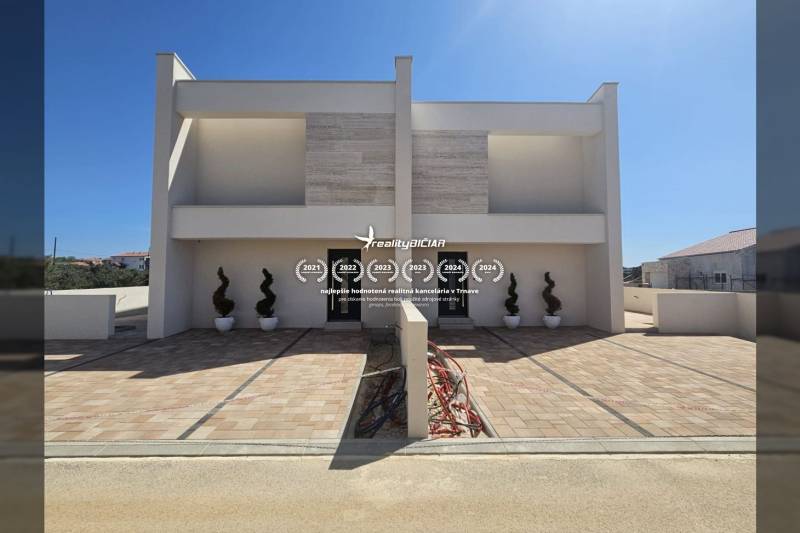 VRSI - dvojdom s bazénom a záhradou - Rodinný dom na ulici Mulo vo Vrsi s dlaždeným chodníkom a dekoratívnymi rastlinami.