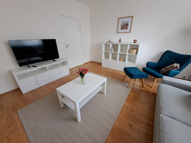 REZERVOVANÉ! Prenajmeme 3-izb. byt, 78 m2, Vráble, okr. Nitra - Obývacia izba v 3-izbovom byte s podlahou s dreveným dekorom a jednoduchým nábytkom.