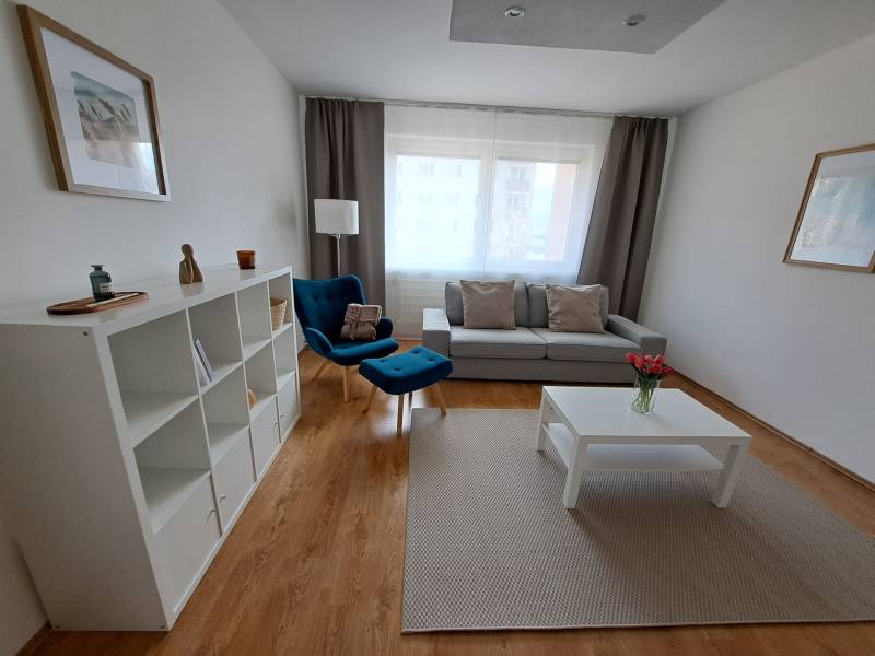 REZERVOVANÉ! Prenajmeme 3-izb. byt, 78 m2, Vráble, okr. Nitra - Obývacia izba v 3-izbovom byte s podlahou s dreveným dekorom, modrým kreslom a bielym nábytkom.