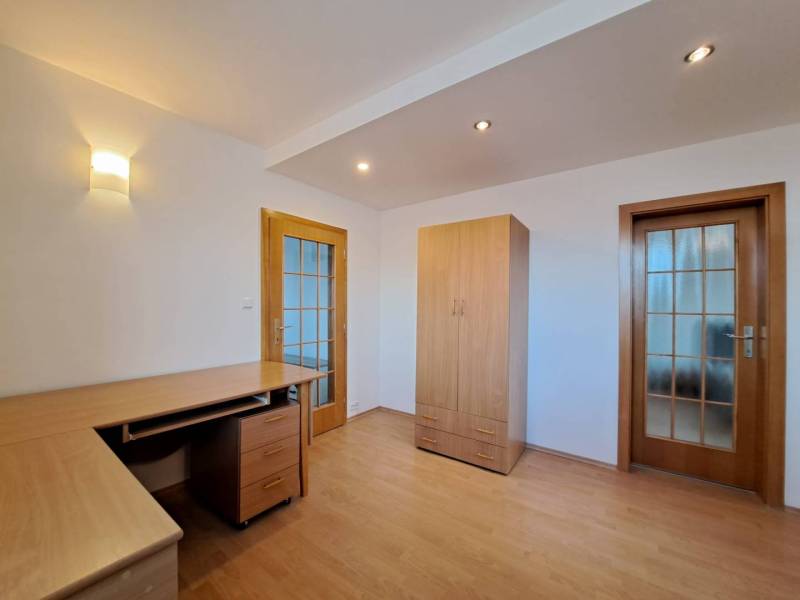 Prenájom pekného a priestranného 4-izbového bytu vo Svite - Izba v 4-izbovom byte s podlahou s dreveným dekorom, stolom a skriňou.