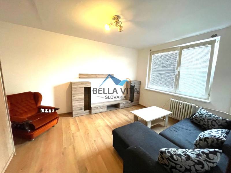 EXKLUZÍVNY PREDAJ - 1 izbový byt Revolučná Štvrť , Galanta - Obývacia izba s podlahou s dreveným dekorom v 1-izbovom byte so sedačkou, kreslom a skriňou.