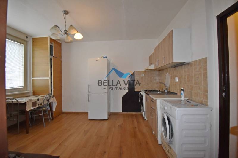 EXKLUZÍVNY PREDAJ - 1 izbový byt Revolučná Štvrť , Galanta - Kuchyňa v 1-izbovom byte s podlahou s dreveným dekorom, jedálenským stolom a spotrebičmi.