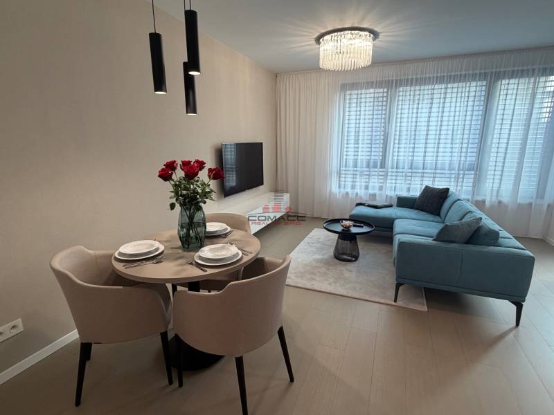 Exk. prenájom lux. 2 iz bytu Rezidencia Blumental - Obývacia izba v 2-izbovom byte s&nbsp;šedou sedačkou, jedálenským stolom a&nbsp;podlahou s dreveným dekorom.