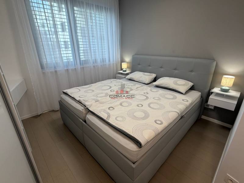 Exk. prenájom lux. 2 iz bytu Rezidencia Blumental - Spálňa v 2-izbovom byte s posteľou, nočnými stolíkmi a podlahou s dreveným dekorom.