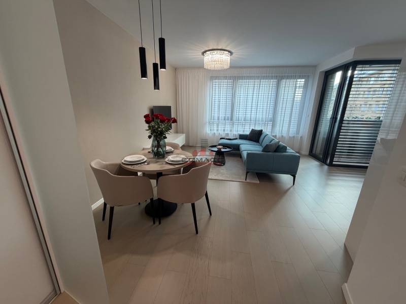 Exk. prenájom lux. 2 iz bytu Rezidencia Blumental - Interiér 2-izbového bytu s podlahou s dreveným dekorom, jedálenským stolom a balkónom.