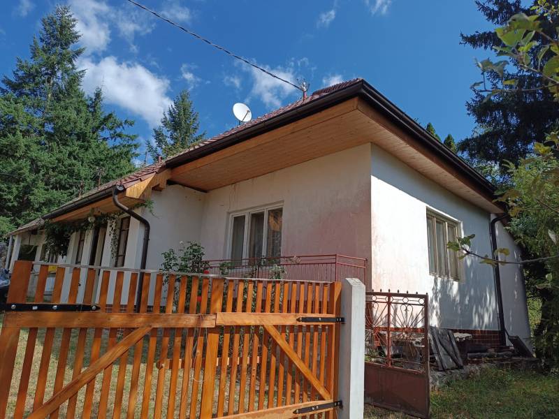 Hospodárska usadlosť s 3,6 hektárovým pozemkom na samote Nová Baňa - Tradičný rodinný dom s dreveným plotom uprostred krásnej prírody a oblohy plnej oblakov.