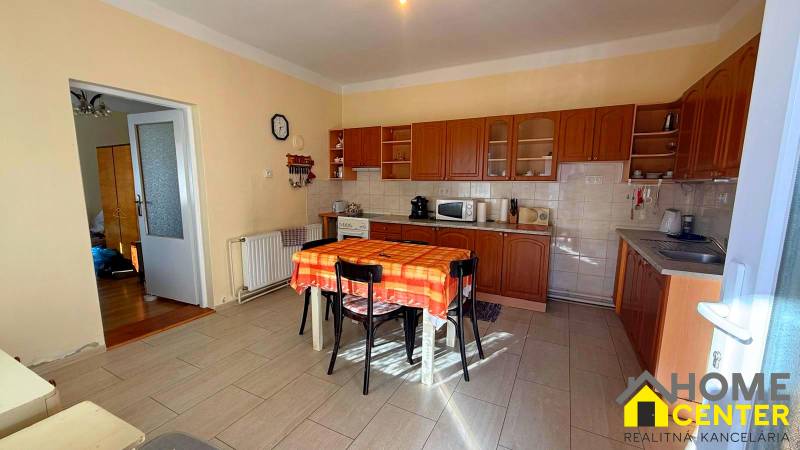 NA PREDAJ 5 izbový rodinný dom s veľkou záhradou v obci Iža - Kuchyňa v rodinnom dome s dreveným dekorom a oranžovým obrusom na stole.