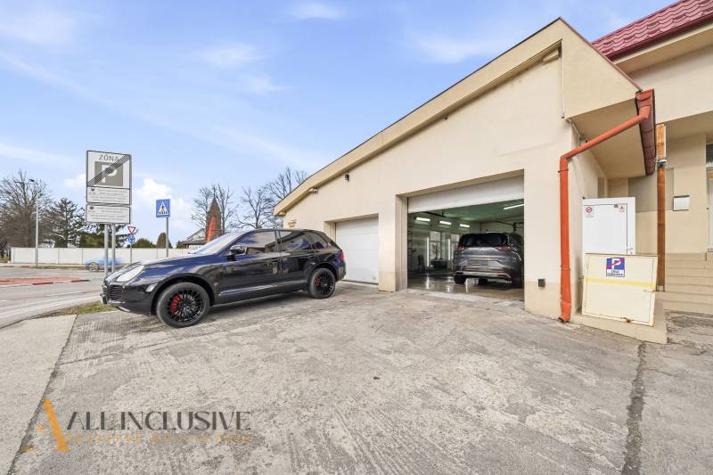 Na predaj 7-izb. RD s obchod. priestorom, Dun. Streda - Budova v Dunajskej Strede s automobilmi pred garážami a dopravnými značkami.