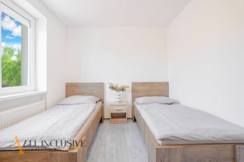 Na predaj 7-izb. RD s obchod. priestorom, Dun. Streda - Izba s dvoma posteľami, nočným stolíkom a podlahou s dreveným dekorom.