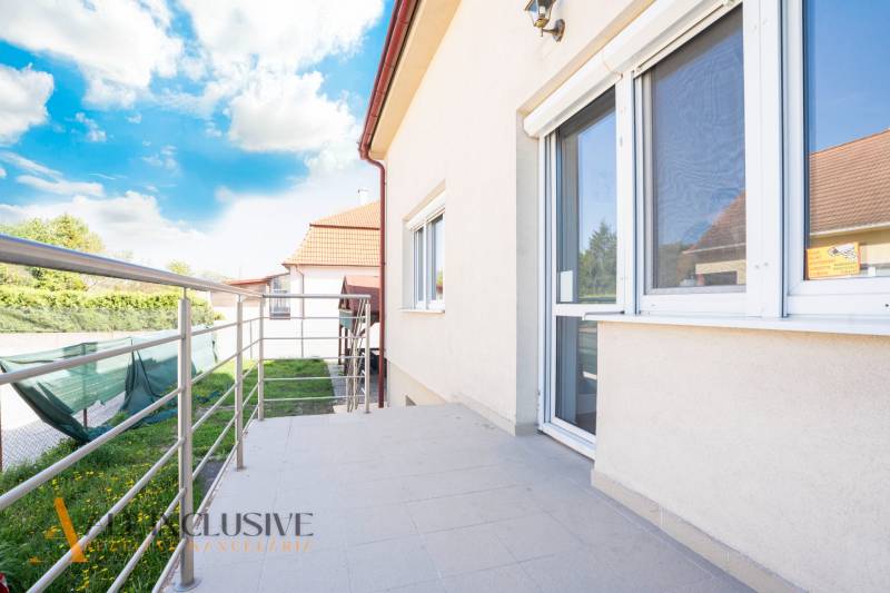 Na predaj 7-izb. RD s obchod. priestorom, Dun. Streda - Budova v Dunajskej Strede s terasou a zábradlím, obloha s oblakmi.