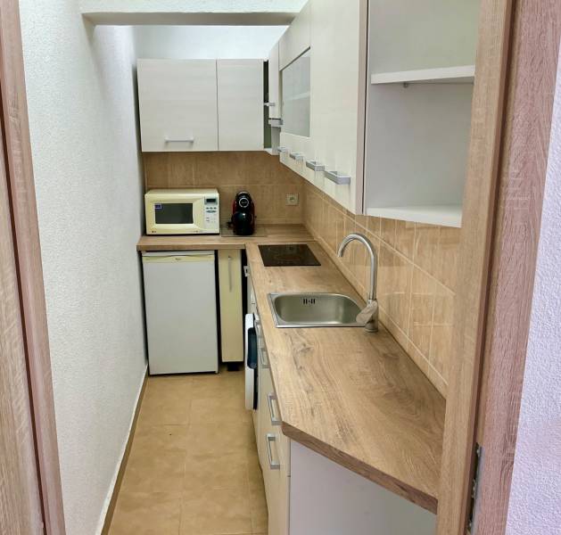 I Predaj Investičného 1-izbového bytu s veľkorysou loggiou  - Kuchyňa v 1-izbovom byte s dreveným dekorom, mikrovlnkou a vstavanými spotrebičmi.