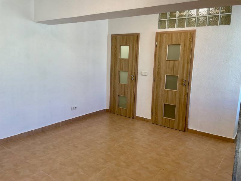 I Predaj Investičného 1-izbového bytu s veľkorysou loggiou  - Interiér 1-izbového bytu s keramickou podlahou a dvoma dverami s dreveným dekorom.