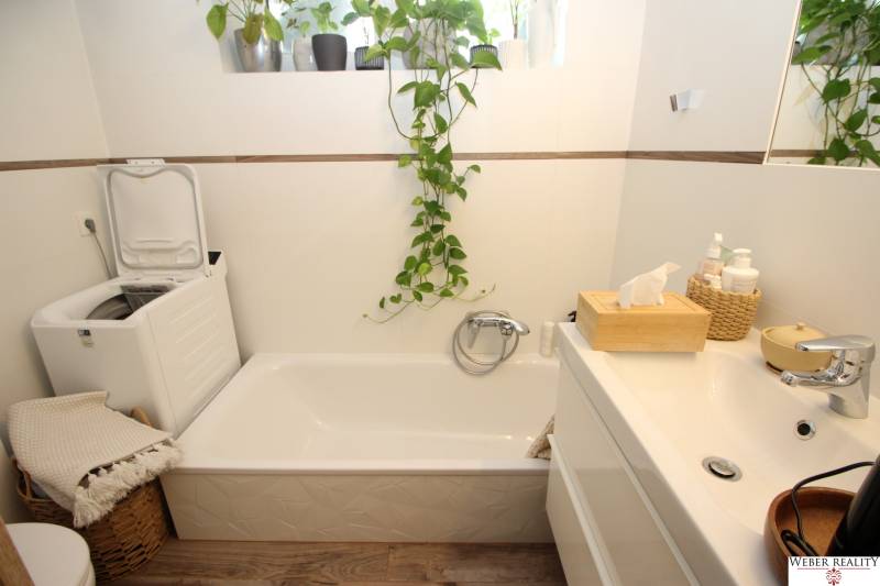 1-izb. kompletne zrekonštr.byt na Hradnom kopci (Lichardova ul.)  - Kúpeľňa v 1-izbovom byte s vaňou, práčkou a dreveným dekorom na podlahe.