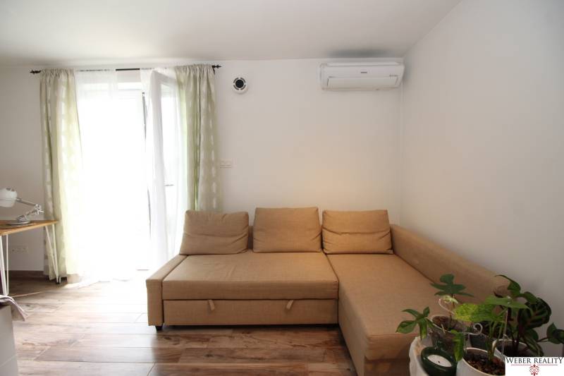 1-izb. kompletne zrekonštr.byt na Hradnom kopci (Lichardova ul.)  - Světlo z okna v 1-izbovom byte so sedačkou, pracovným stolom a podlahou s dreveným dekorom.