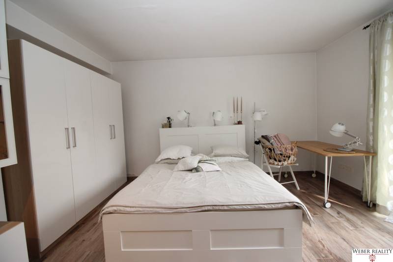 1-izb. kompletne zrekonštr.byt na Hradnom kopci (Lichardova ul.)  - Spálňa v 1-izbovom byte s posteľou, bielou skriňou a podlahou s dreveným dekorom.