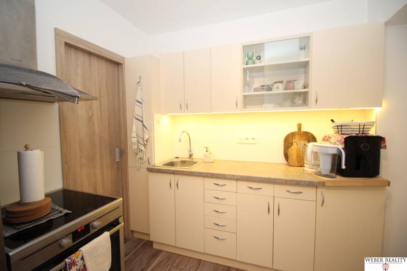 1-izb. kompletne zrekonštr.byt na Hradnom kopci (Lichardova ul.)  - Kuchyňa v 1-izbovom byte so svetlým nábytkom a podlahou s dreveným dekorom.