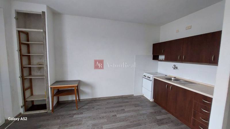 PREDAJ: 1 izbový byt - 37m2, s loggiou, Ružomberok - Za dráhou - Kuchyňa v 1-izbovom byte s tmavými skrinkami a podlahou s dreveným dekorom.