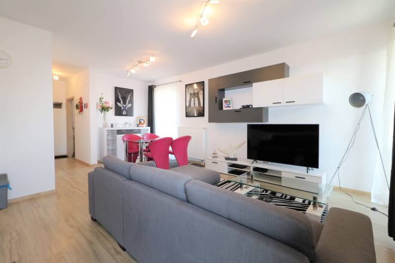 NUERA︱ SLNEČNICE- slnečný 2izbový byt s výhľadom na hrad - Obývacia izba v 2-izbovom byte so sivou sedačkou, podlahou s dreveným dekorom a televízorom.