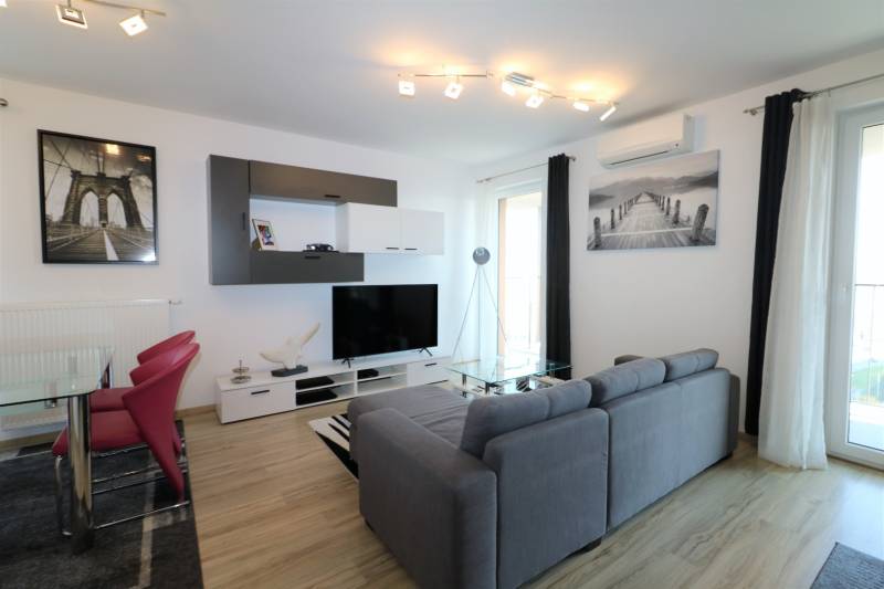 NUERA︱ SLNEČNICE- slnečný 2izbový byt s výhľadom na hrad - Obývacia izba v 2-izbovom byte s pohovkou, TV, podlahou s dreveným dekorom.