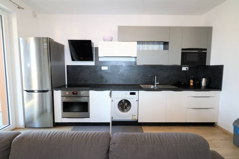 NUERA︱ SLNEČNICE- slnečný 2izbový byt s výhľadom na hrad - Kuchyňa v 2-izbovom byte so sivými skrinkami, spotrebičmi a podlahou s dreveným dekorom.