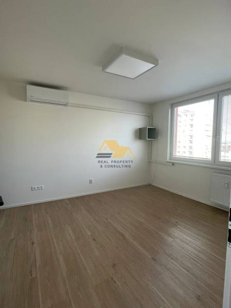 Prenajmem 1 izbový byt na Nábrežnej ulici v Nových Zámkoch - Izba s bielymi stenami a podlahou s dreveným dekorom v 1-izbovom byte.