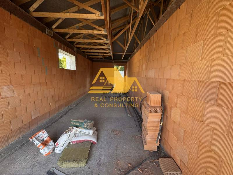 Predám novostavbu rodinného domu s garážou v Nových Zámkoch - Stavba rodinného domu na ulici v Nových Zámkoch s tehlovými stenami a trámovým stropom.