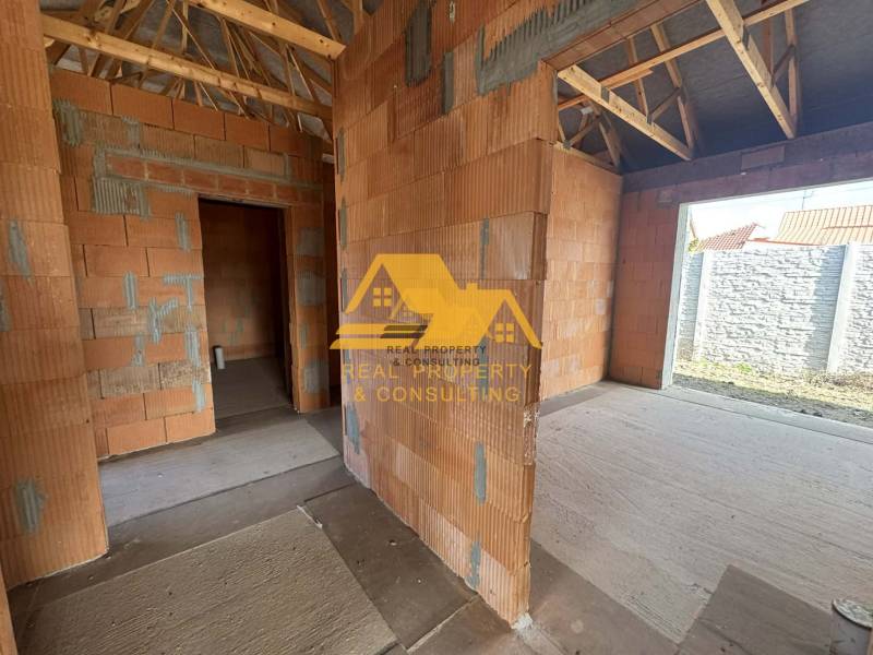 Predám novostavbu rodinného domu s garážou v Nových Zámkoch - Rozostavaný rodinný dom s pohľadom na steny bez omietky a dreveným krovom.