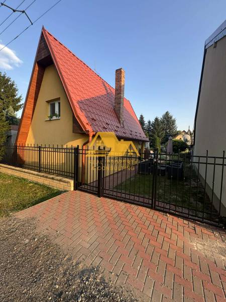 Predám peknú chatu na celoročné bývanie v Nových zámkoch - Chata na ulici v Nových Zámkoch, so špicatou strechou a tehlovým komínom.