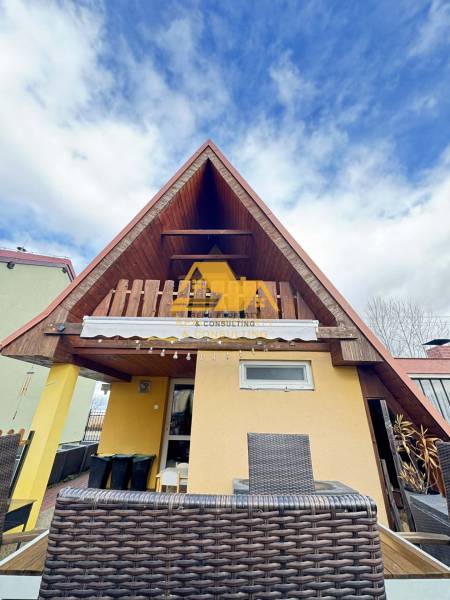 Predám peknú chatu na celoročné bývanie v Nových zámkoch - Drevená chata s terasou v Nových Zámkoch pod modrým oblohou.