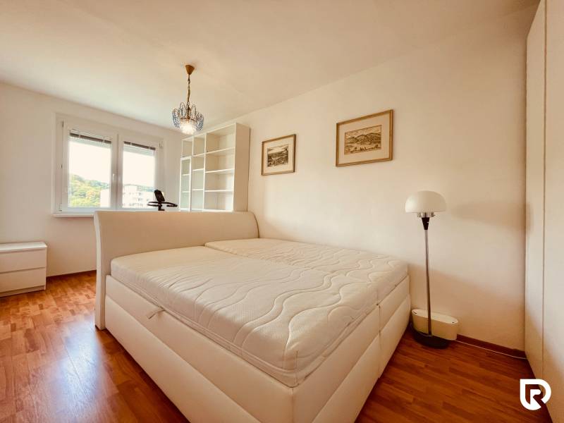 EXKLUZÍVNE! | Krásny 2-izbový byt | 52m² | Považanova - Svetlá spálňa v 2-izbovom byte s podlahou s dreveným dekorom a veľkým oknom.