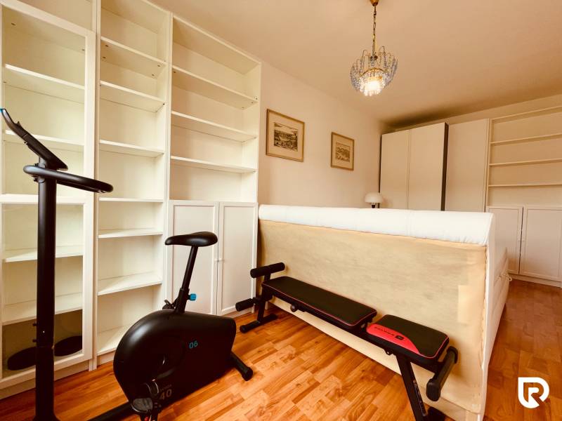 EXKLUZÍVNE! | Krásny 2-izbový byt | 52m² | Považanova - Izba s rotopedom v 2-izbovom byte, biele police, podlaha s dreveným dekorom.