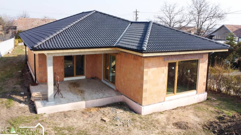 PRIESTRANNÁ 4-IZBOVÁ NOVOSTAVBA 167.38m²- BUNGALOV NA POZEMKU AŽ 702m² - Rodinný dom v Pavliciach s čiernou strechou a terasou v záhrade.