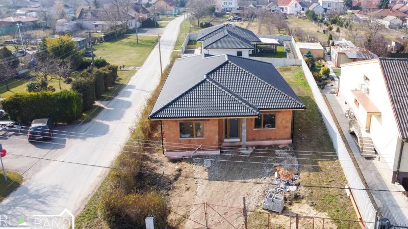 PRIESTRANNÁ 4-IZBOVÁ NOVOSTAVBA 167.38m²- BUNGALOV NA POZEMKU AŽ 702m² - Rodinný dom v Pavliciach so strechou z čiernych škridiel na trávnatom pozemku.