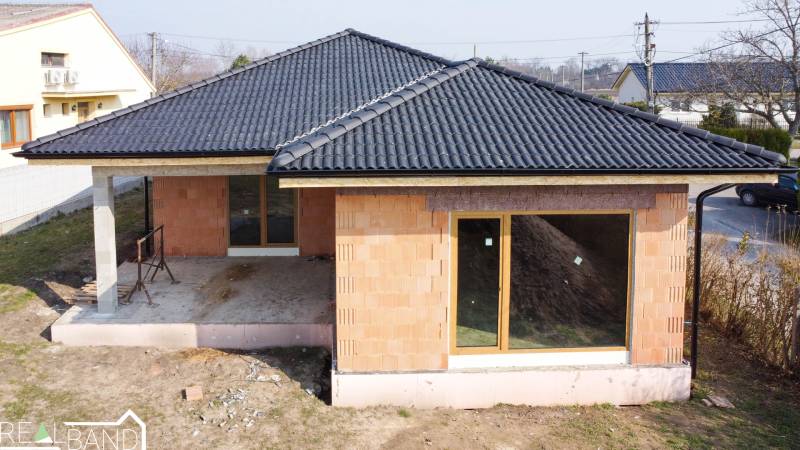 PRIESTRANNÁ 4-IZBOVÁ NOVOSTAVBA 167.38m²- BUNGALOV NA POZEMKU AŽ 702m² - Rodinný dom v Pavliciach vo výstavbe, tehlová fasáda, tmavá strecha, veľké okná.