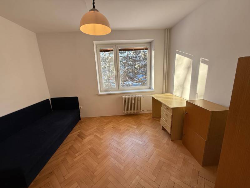 Ponúkame na prenájom priestranný 3-izbový byt v centre Martina  - Izba v 3-izbovom byte s podlahou s dreveným dekorom, modrou pohovkou a písacím stolom.