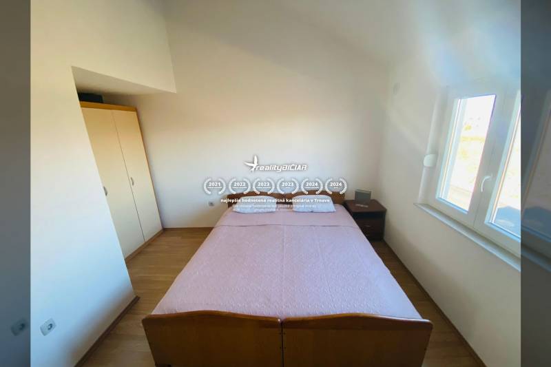 NIN-GRBLJANSKE VIKENDICE - dom s dvoma bytmi - Spálňa v rodinnom dome s posteľou, nočným stolíkom a podlahou s dreveným dekorom.